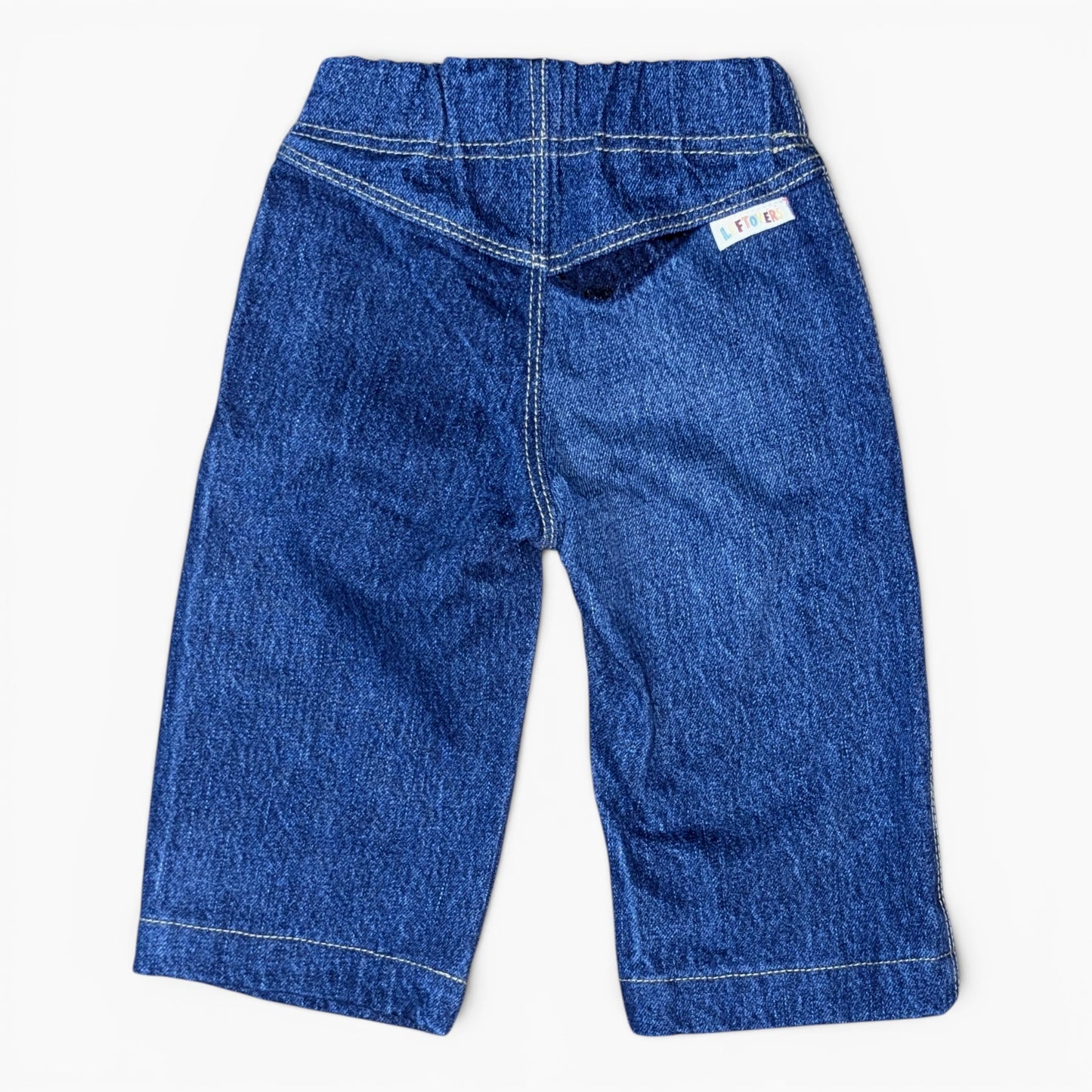 A pair of blue denim toddler pants shown from the back, featuring a wide elastic waistband, contrast white stitching, and a small white brand tag on the upper right side.