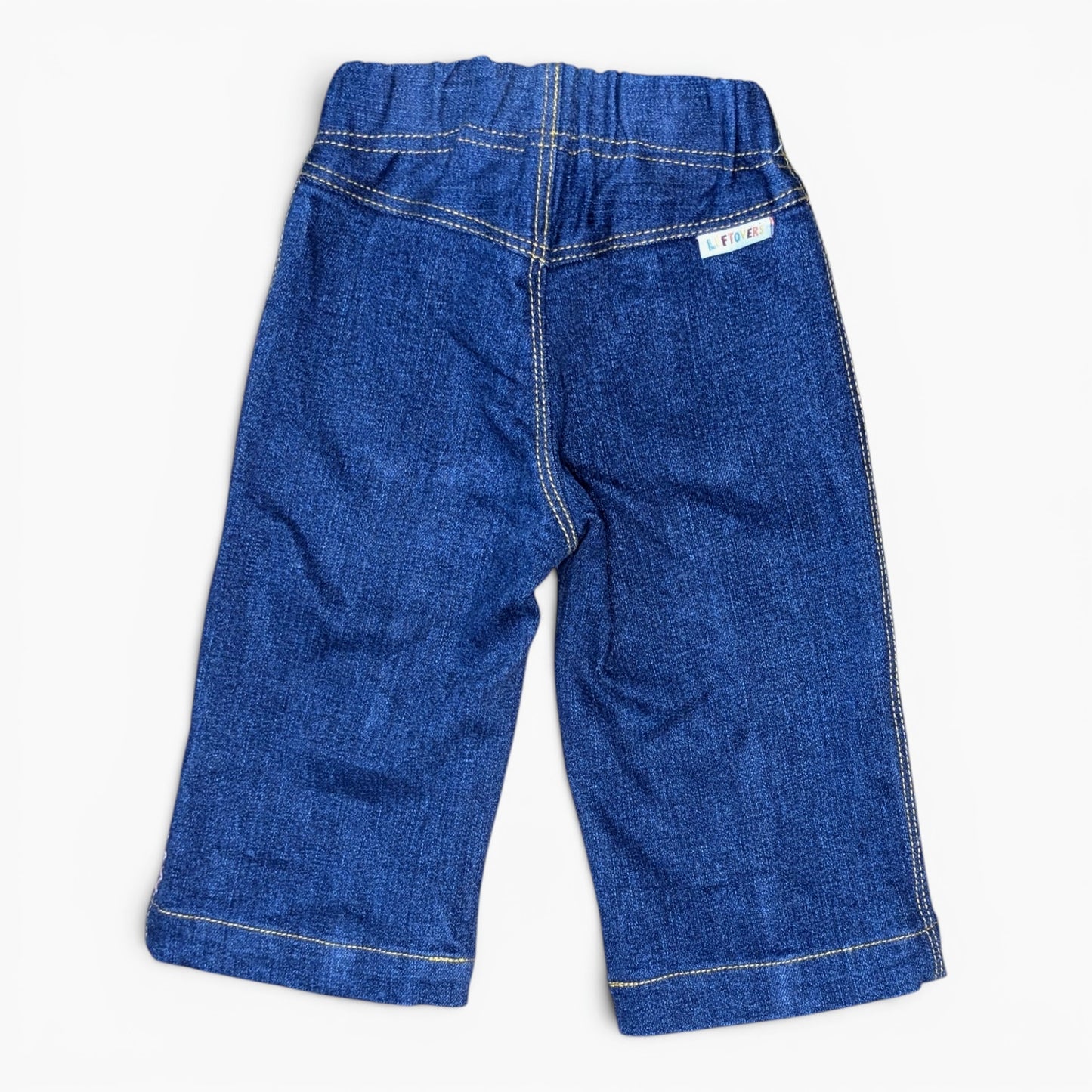 A pair of blue denim pants shown from the back, featuring a wide elastic waistband, contrast light-colored stitching, and a small white brand label on the upper right side.