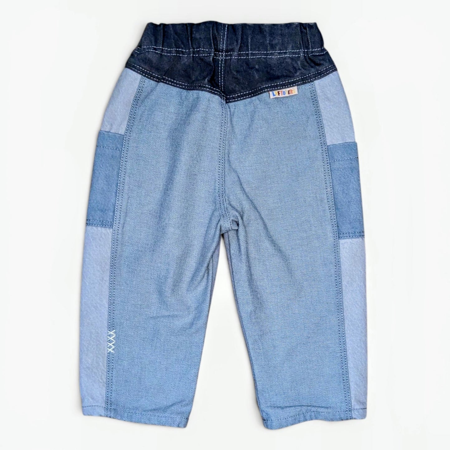 A pair of children's patchwork denim pants in shades of light and dark blue, laid flat against a white background.