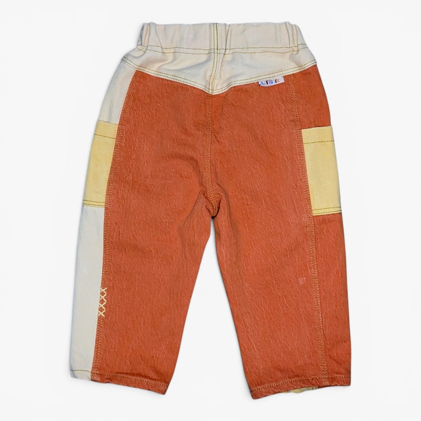 A pair of children's patchwork pants in orange, beige, and cream, laid flat against a white background.