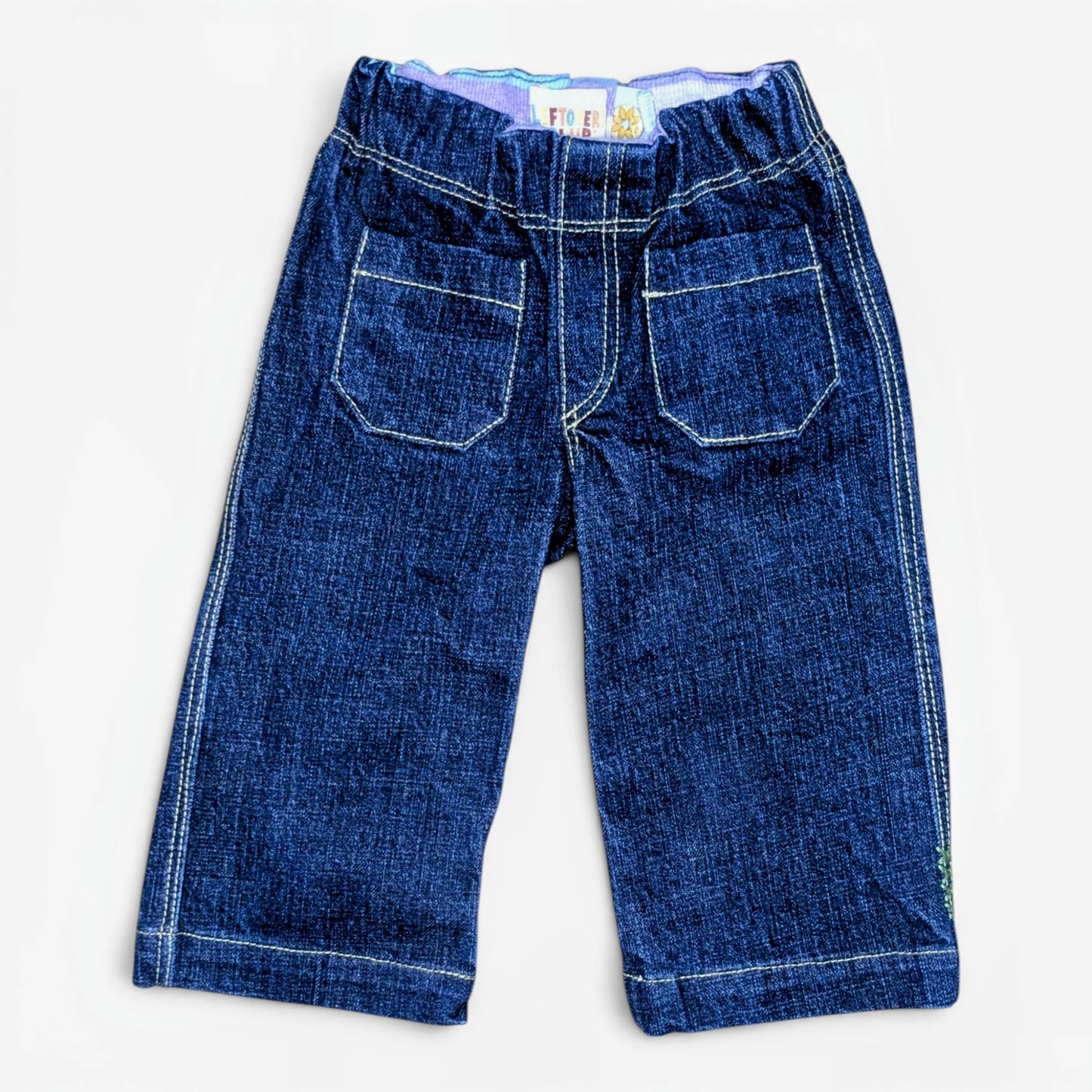 A pair of dark blue denim pants with white contrast stitching, featuring two large patch pockets on the back, laid flat against a white background.