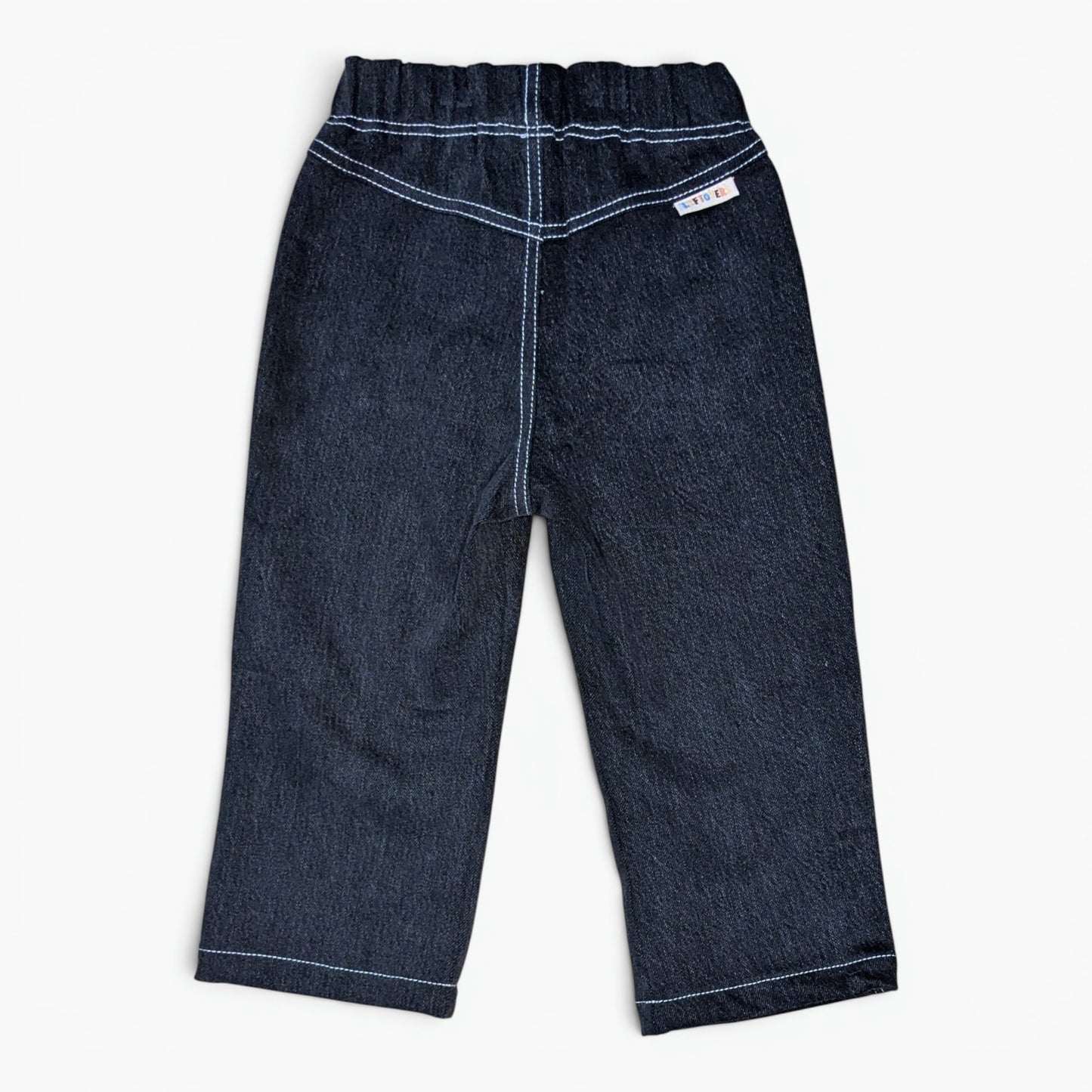 A pair of black denim pants for toddlers, shown from the back on a clean white background. The pants feature a wide elastic waistband, double-stitched contrast stitching in white thread, and a small white brand label on the upper right side.