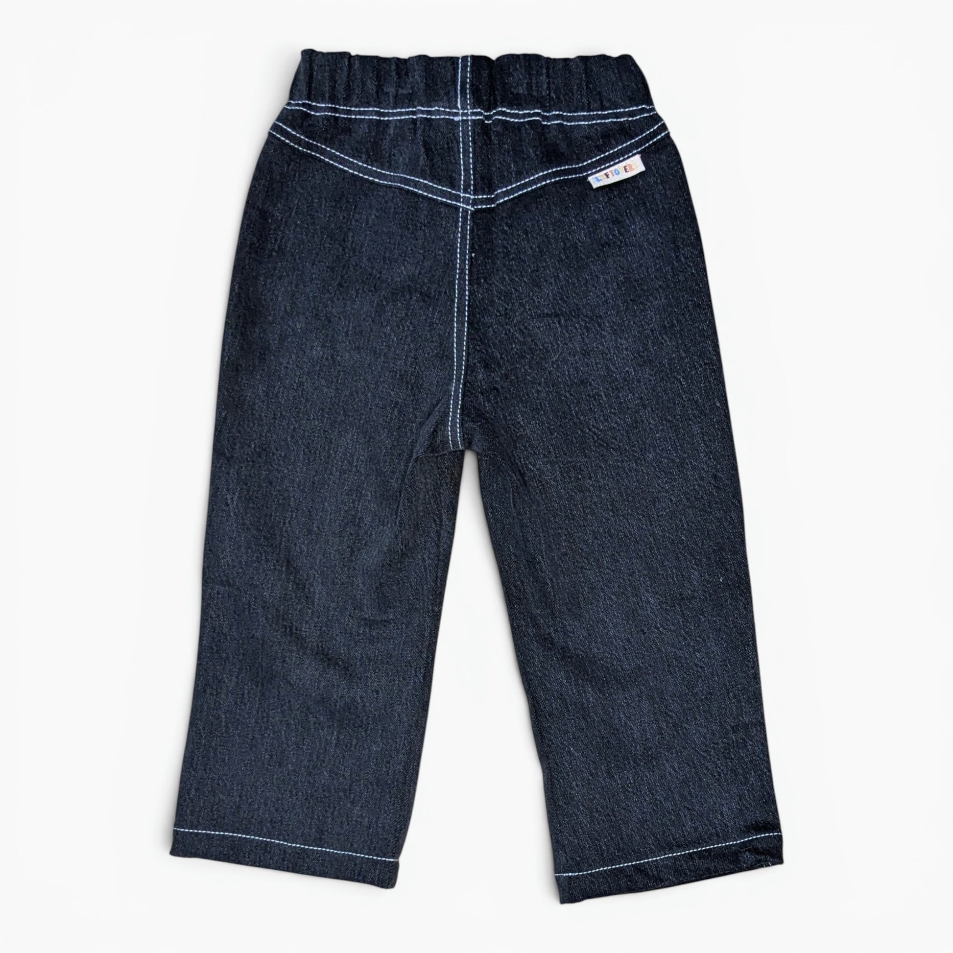 A pair of black denim pants for toddlers, shown from the back on a clean white background. The pants feature a wide elastic waistband, double-stitched contrast stitching in white thread, and a small white brand label on the upper right side.