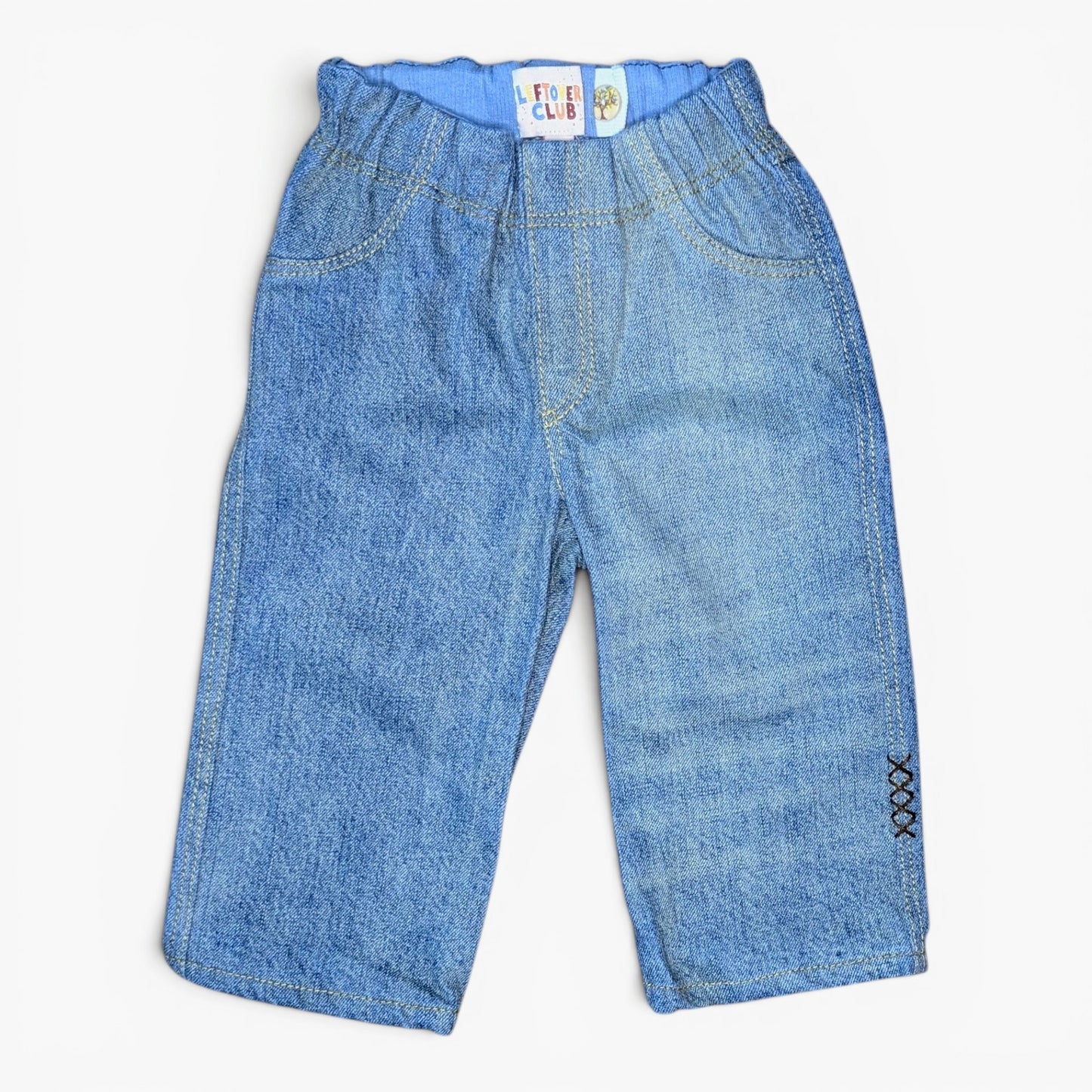 Light blue denim capri pants for toddlers, featuring an elastic waistband, front patch pockets, and decorative black cross stitch detailing on the lower left leg.