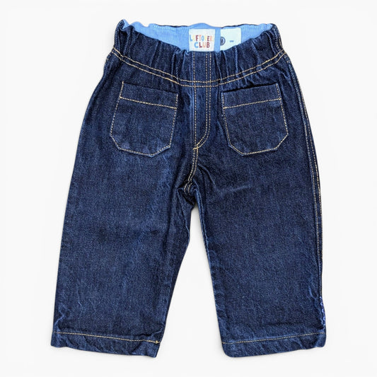 A pair of dark blue denim shorts for toddlers, featuring an elastic waistband, two back patch pockets, and contrast light-colored stitching, shown flat on a white background.