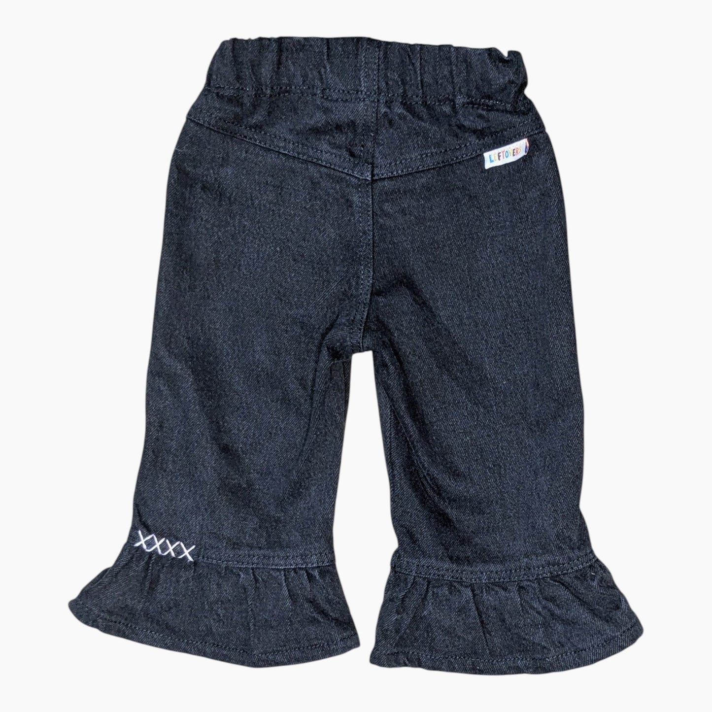 Dark indigo denim shorts for toddlers, featuring an elastic waistband, ruffled hems, and white embroidered details on the back pocket and lower leg.