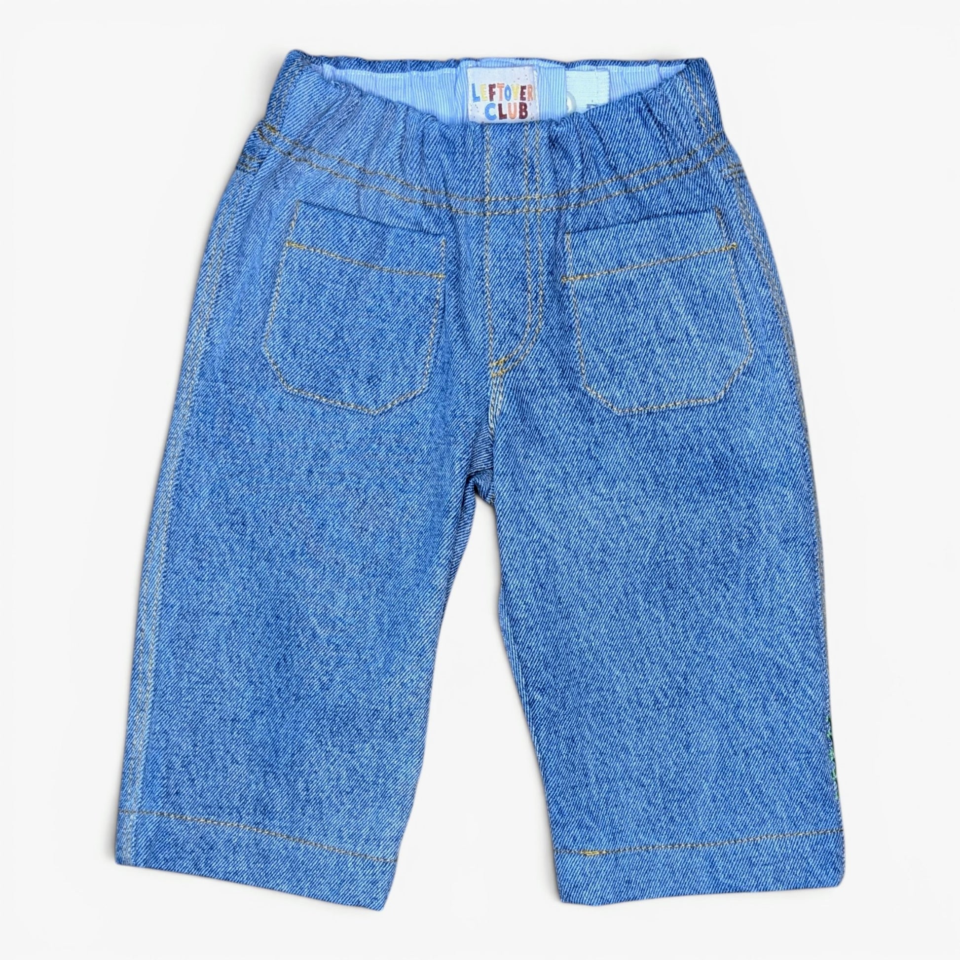 A pair of blue denim pants for kids, shown from the back with an elastic waistband, dual back pockets, and contrast stitching, laid flat on a white background.