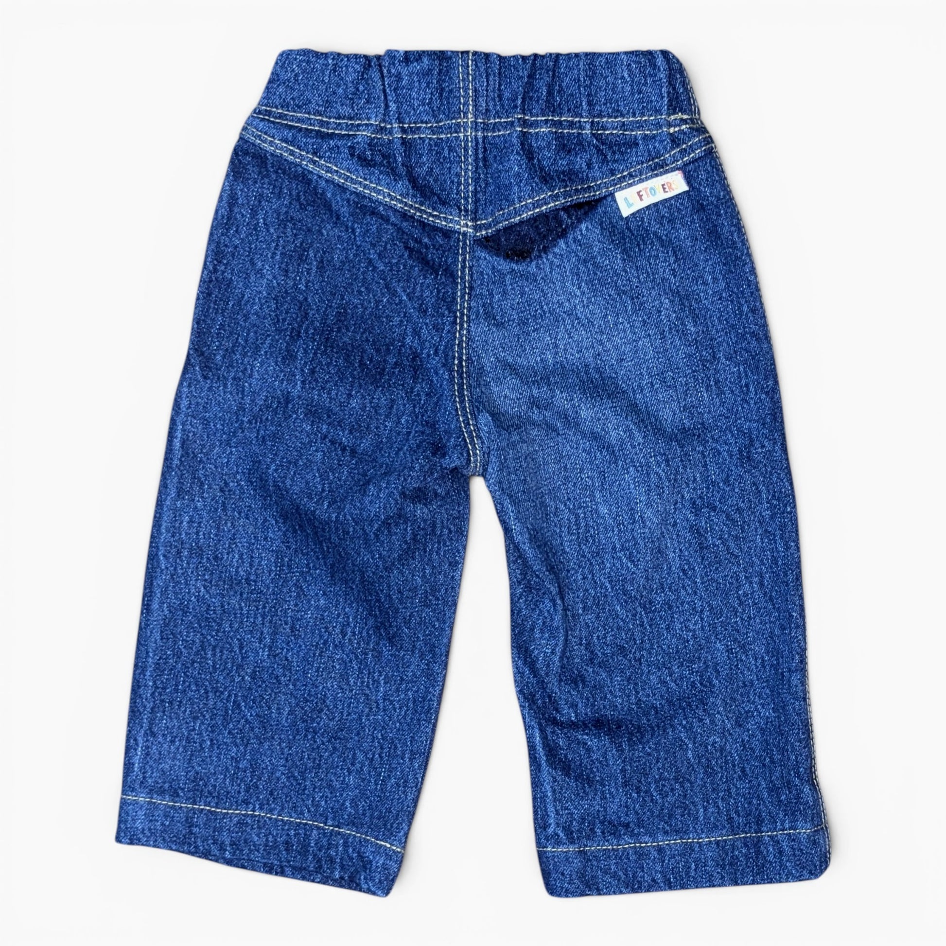 A pair of blue denim toddler pants shown from the back, featuring a wide elastic waistband, contrast white stitching, and a small white brand tag on the upper right side.