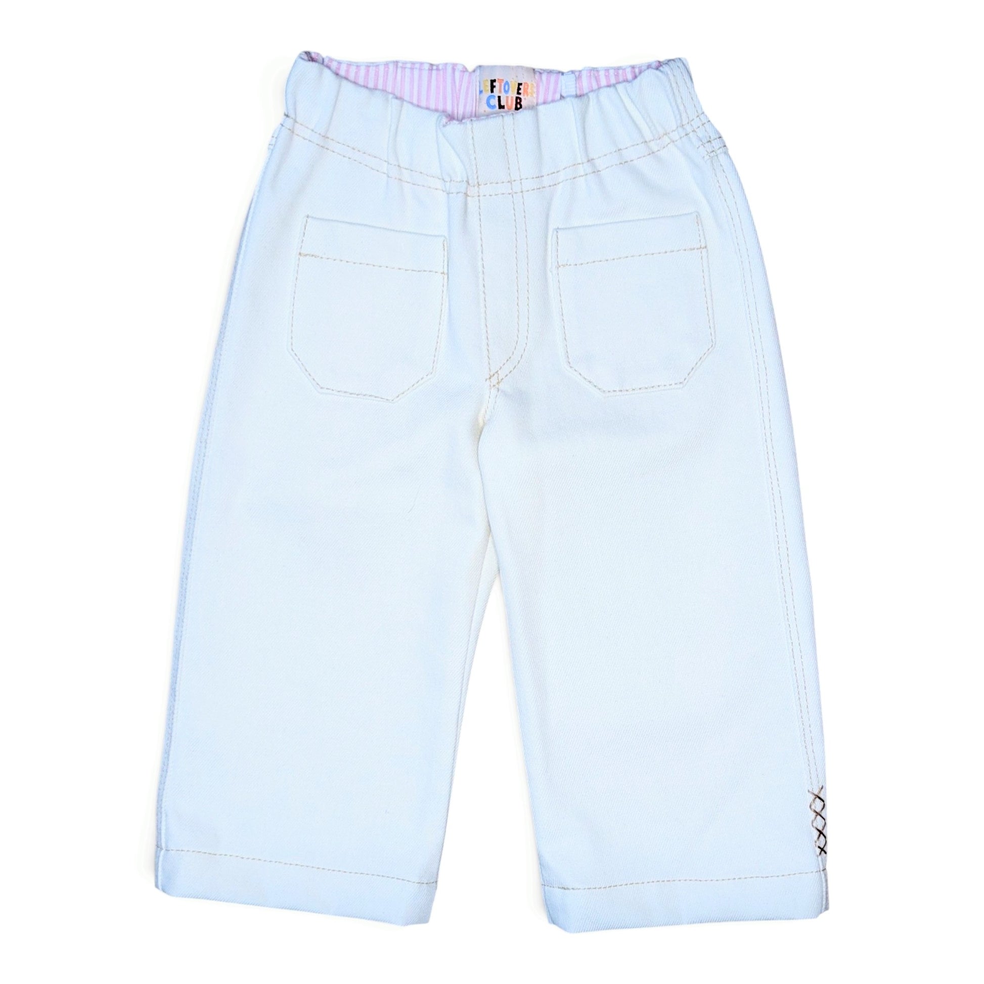 A pair of white denim pants for kids, shown from the back. The pants feature an elastic waistband with a pink and white striped inner lining, two large patch pockets, and contrast stitching.
