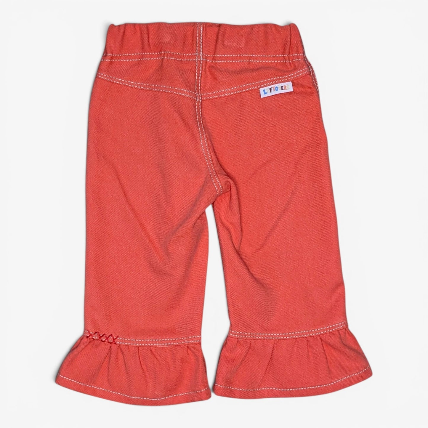 A pair of toddler's coral red denim capri pants with ruffled hems and white contrast stitching, shown flat against a light gray background.