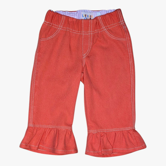 A pair of toddler's denim pants in a muted red-orange color, featuring white contrast stitching, and ruffled hems, shown against a plain white background.