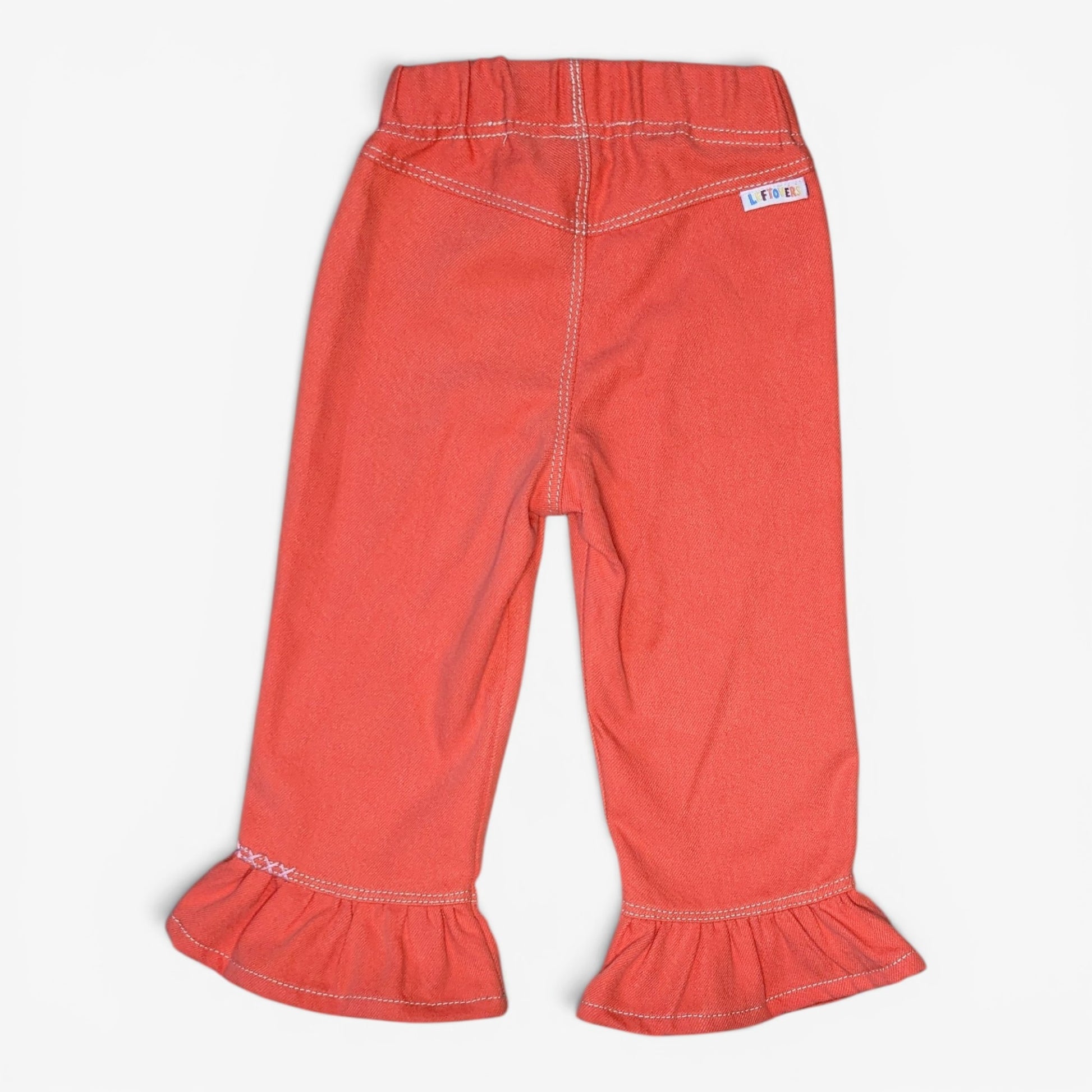 A pair of toddler's coral orange denim pants with ruffled hems and contrast white stitching, shown flat on a light gray background.