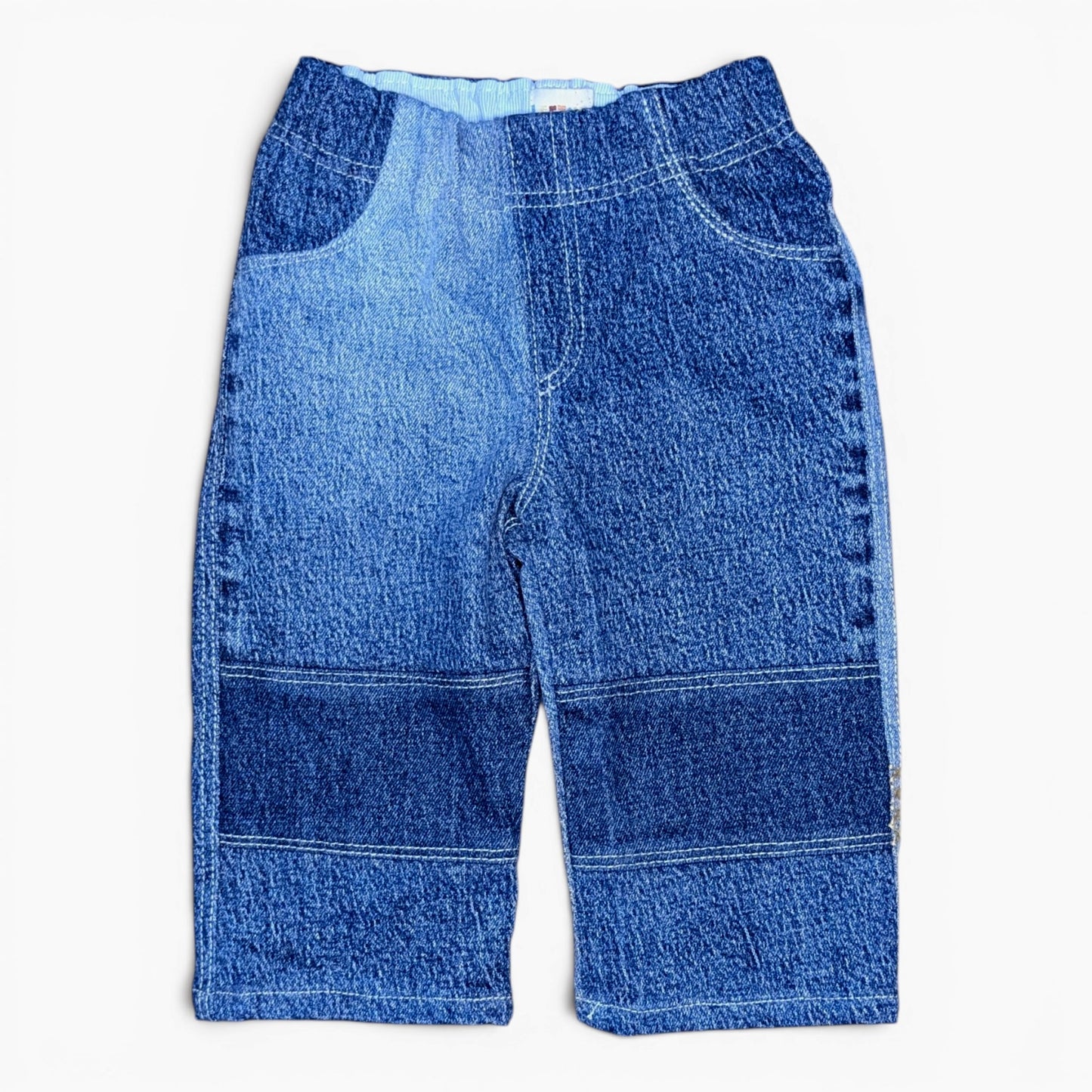 A pair of blue denim pants with a patchwork design of different blue washes, laid flat against a white background.