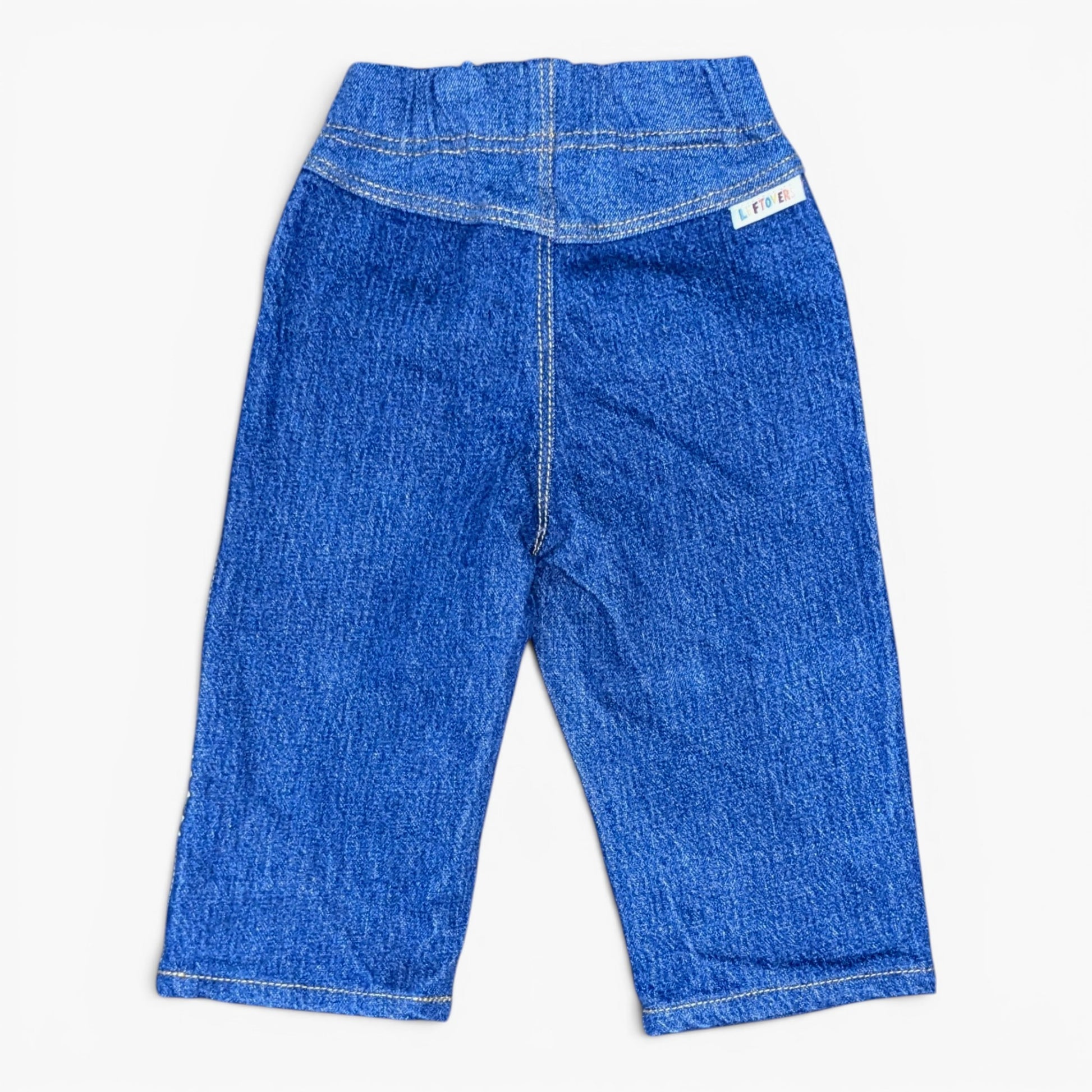 Blue denim pants shown from the back, featuring a wide elastic waistband, a central seam, and a small white brand tag on the upper right side, laid flat against a light background.