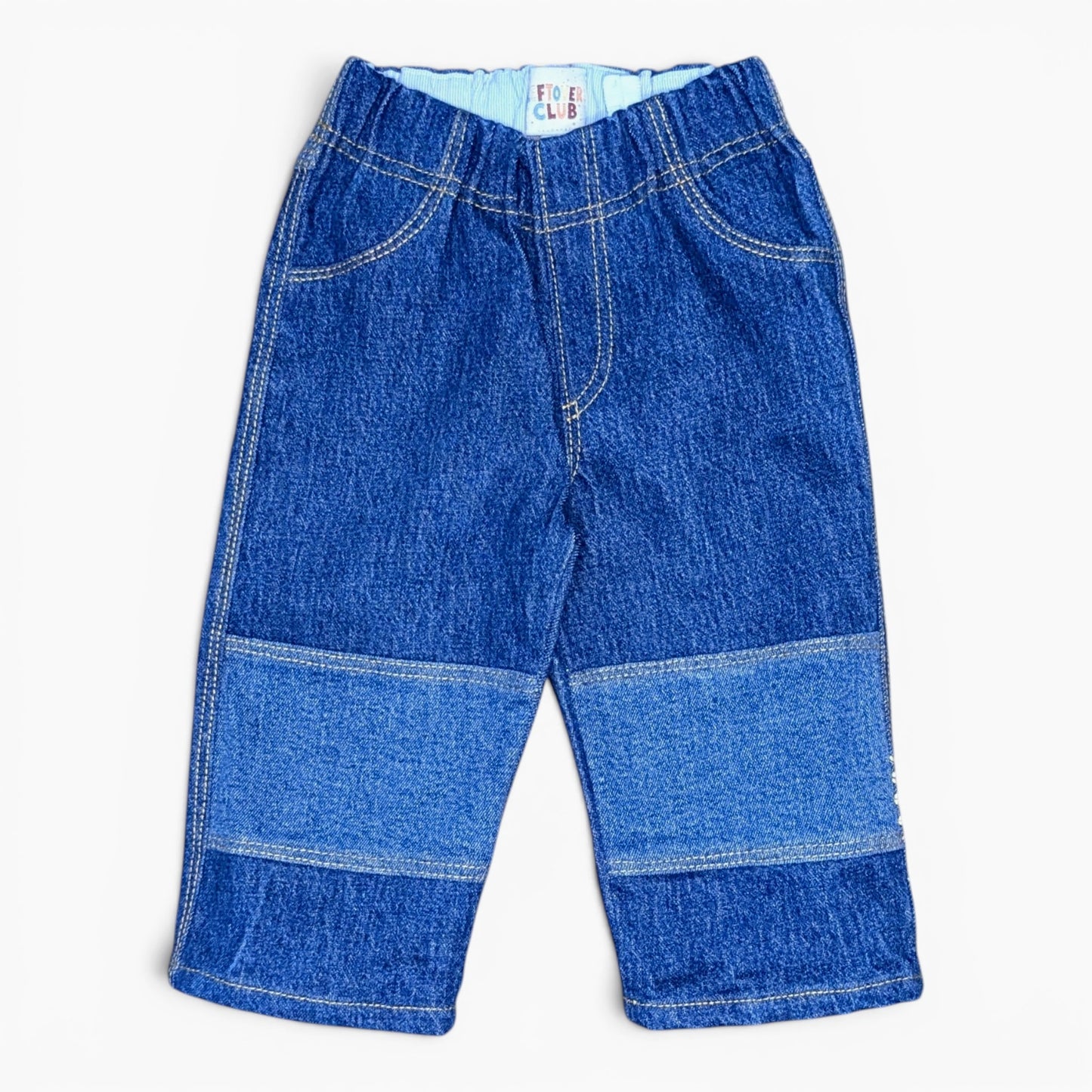 A pair of toddler denim pants in a blue wash, featuring horizontal patchwork panels on the lower legs and contrast light blue lining at the elastic waistband, shown flat on a white background.