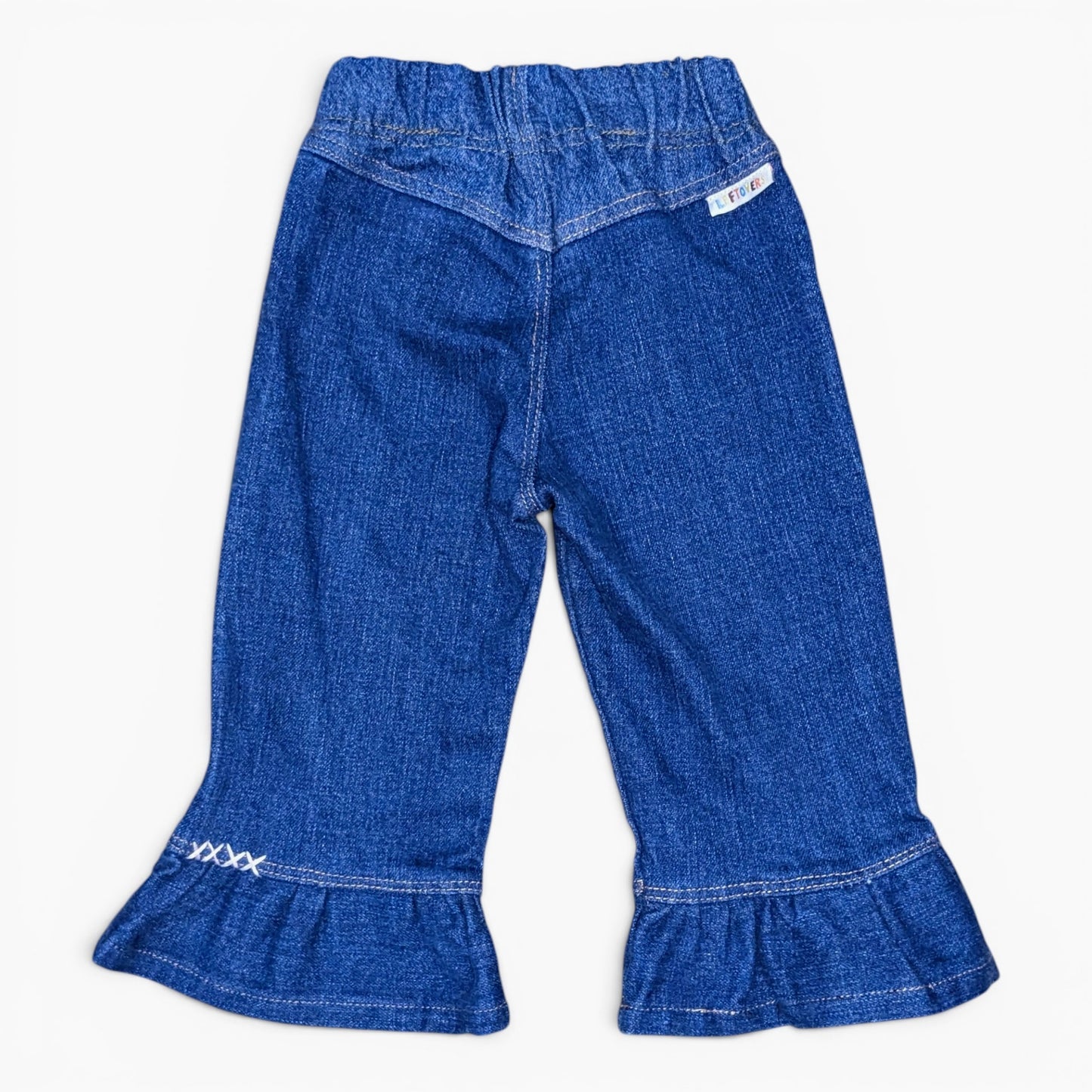 A pair of toddler blue denim bell-bottom pants with a ruffled hem and a white embroidered logo on the left cuff, shown against a plain white background.