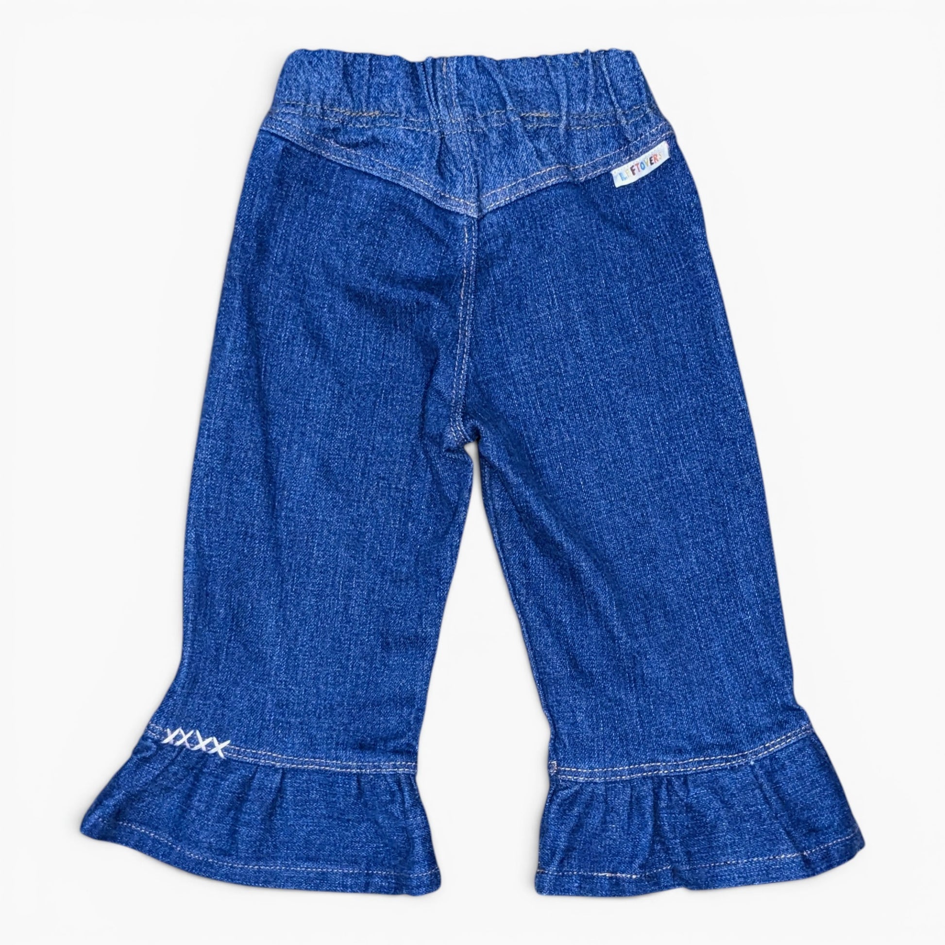 A pair of toddler blue denim bell-bottom pants with a ruffled hem and a white embroidered logo on the left cuff, shown against a plain white background.