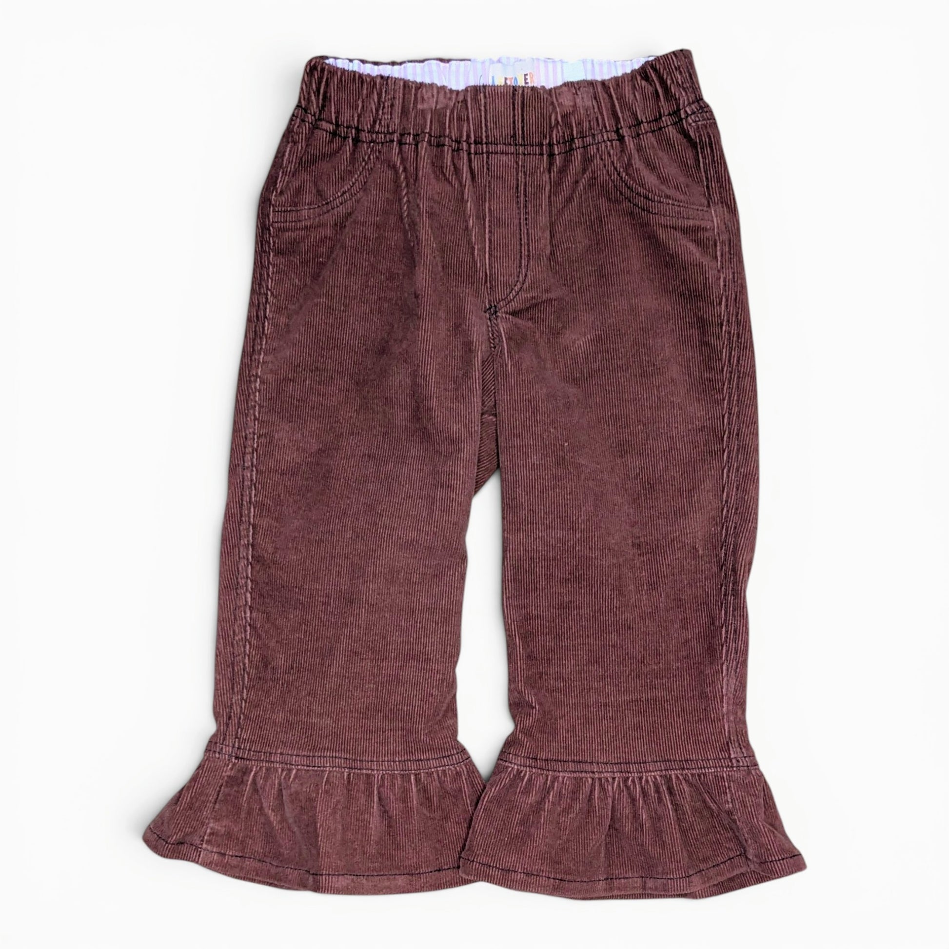 A pair of toddler's corduroy pants in a dusty rose or mauve-brown color, featuring an elastic waistband and ruffled hems, laid flat against a white background.