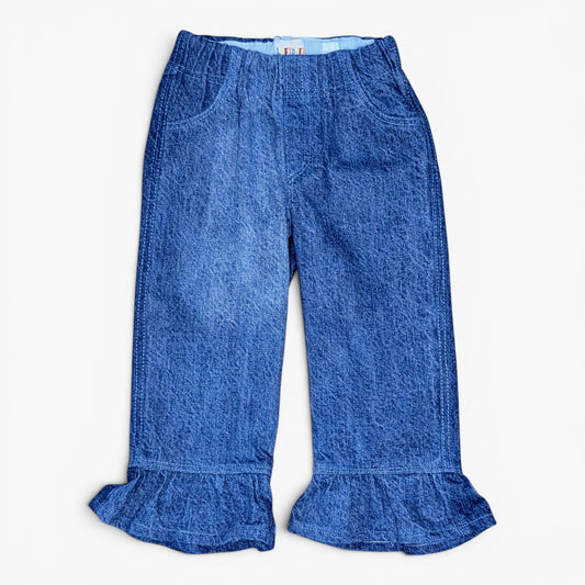 A pair of blue denim pants with a ruffled hem and front pockets, laid flat against a light off-white background.