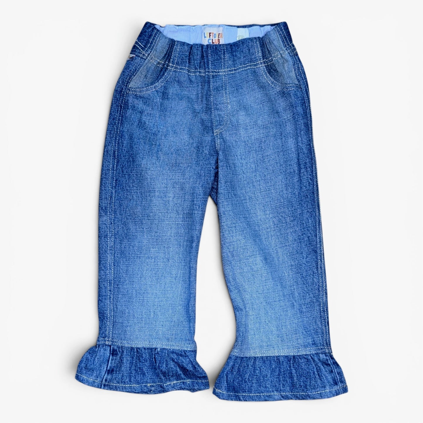 A pair of blue denim pants with a wide elastic waistband and ruffled hems, shown flat on a light gray background.
