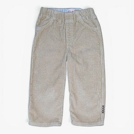 A pair of beige corduroy pants for toddlers, featuring an elastic waistband, front pockets, and a small black embroidered 'XX' detail on the lower left leg, shown against a plain white background.