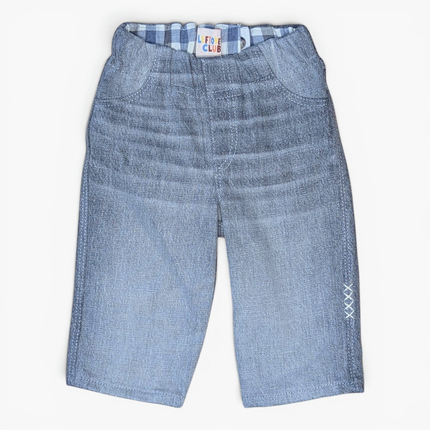 Light grey denim pants for toddlers, featuring a gusseted front pocket design, elastic waistband with a blue and white checkered lining, and white embroidered 'XXX' details on the lower left leg.