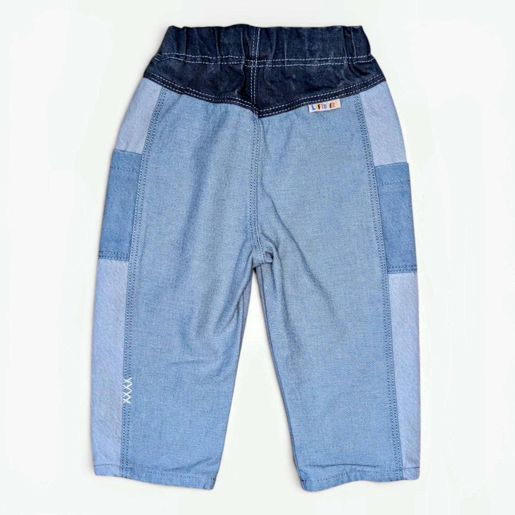 A pair of children's patchwork denim pants in shades of light and dark blue, laid flat against a white background.