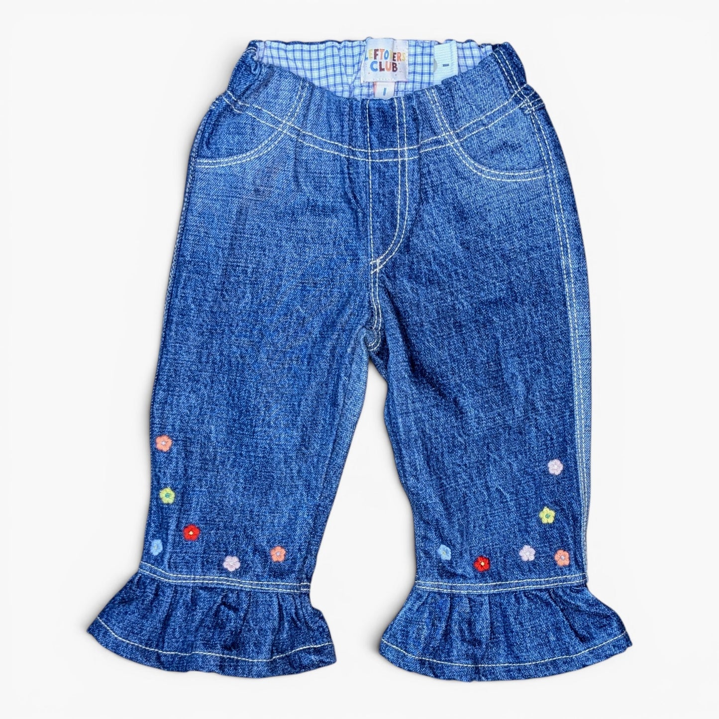 Blue denim pants for toddlers, featuring a gingham waistband, decorative colorful embroidered flowers near the ruffled hems, and contrast white stitching.