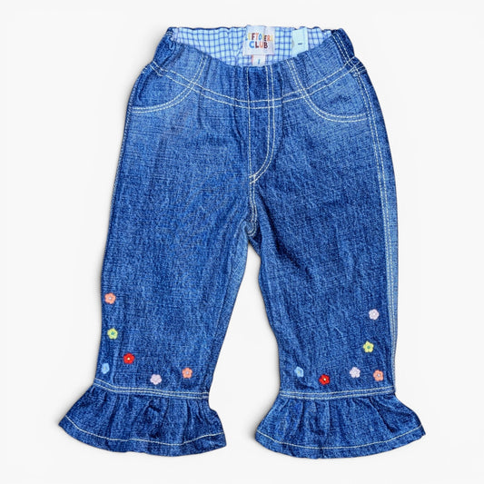 Blue denim pants for toddlers, featuring a gingham waistband, decorative colorful embroidered flowers near the ruffled hems, and contrast white stitching.