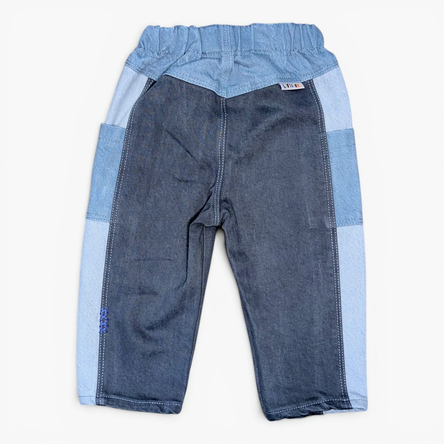A pair of children's patchwork denim pants in shades of blue, featuring a dark blue front panel and light blue side panels, laid flat against a white background.