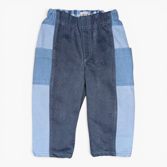 A pair of patchwork denim pants for toddlers, featuring a dark blue denim front panel and light blue denim side panels and pockets, laid flat against a white background.