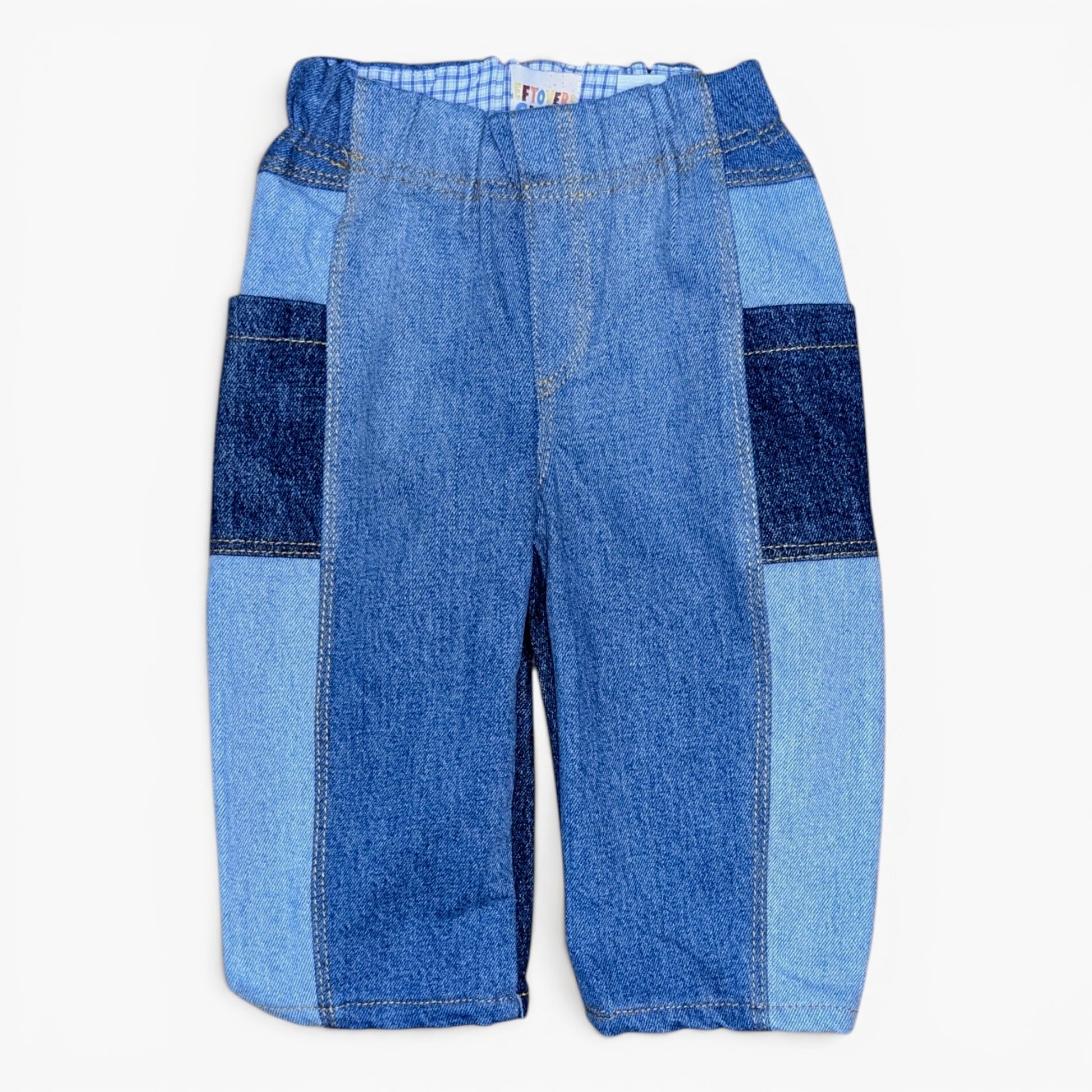 A pair of patchwork denim pants in various shades of blue, featuring a central lighter blue denim panel, darker blue denim side panels, and a subtle striped pattern at the elastic waistband, shown flat on a white background.