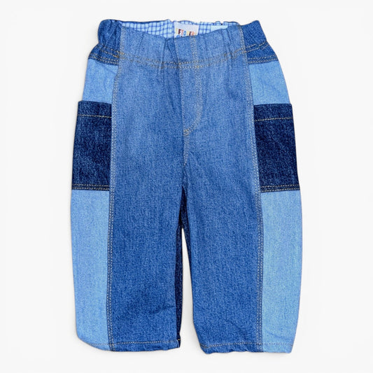 A pair of patchwork denim pants in various shades of blue, featuring a central lighter blue denim panel, darker blue denim side panels, and a subtle striped pattern at the elastic waistband, shown flat on a white background.