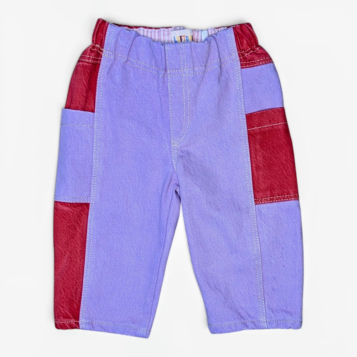 A pair of children's patchwork pants in lavender and red, laid flat against a light off-white background.