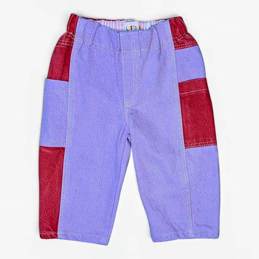 A pair of children's patchwork pants in lavender and red, laid flat against a light off-white background.
