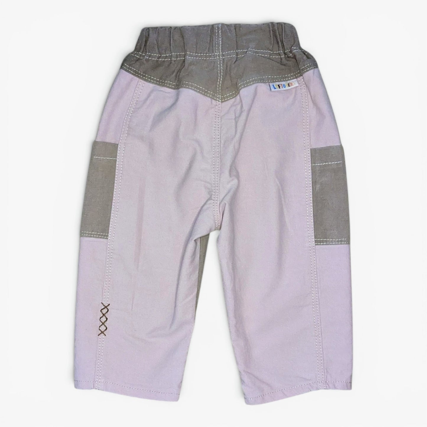 A pair of children's shorts in brown and pink panels, featuring an elastic waistband and a small decorative embroidered 'X' on one leg.