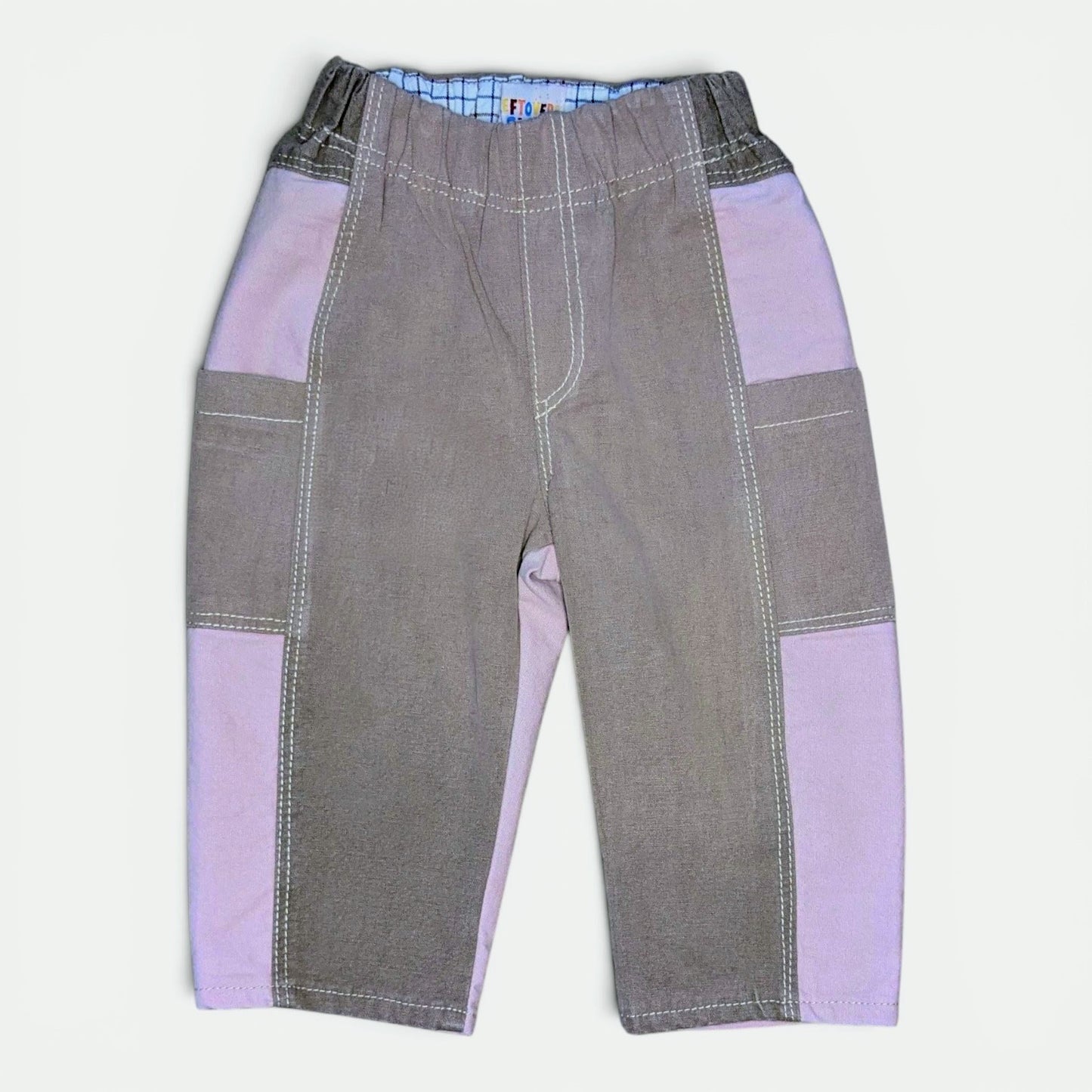 A pair of patchwork-style pants for toddlers, featuring brown and pink panels on the sides and upper thighs, finished with white contrast stitching.