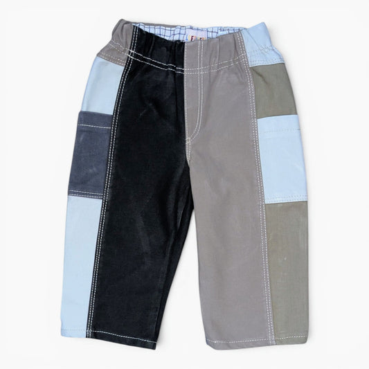 A pair of patchwork patchwork pants for kids, featuring panels of black corduroy, gray fabric, light blue denim, and olive green canvas with white contrast stitching, shown against a plain white background.