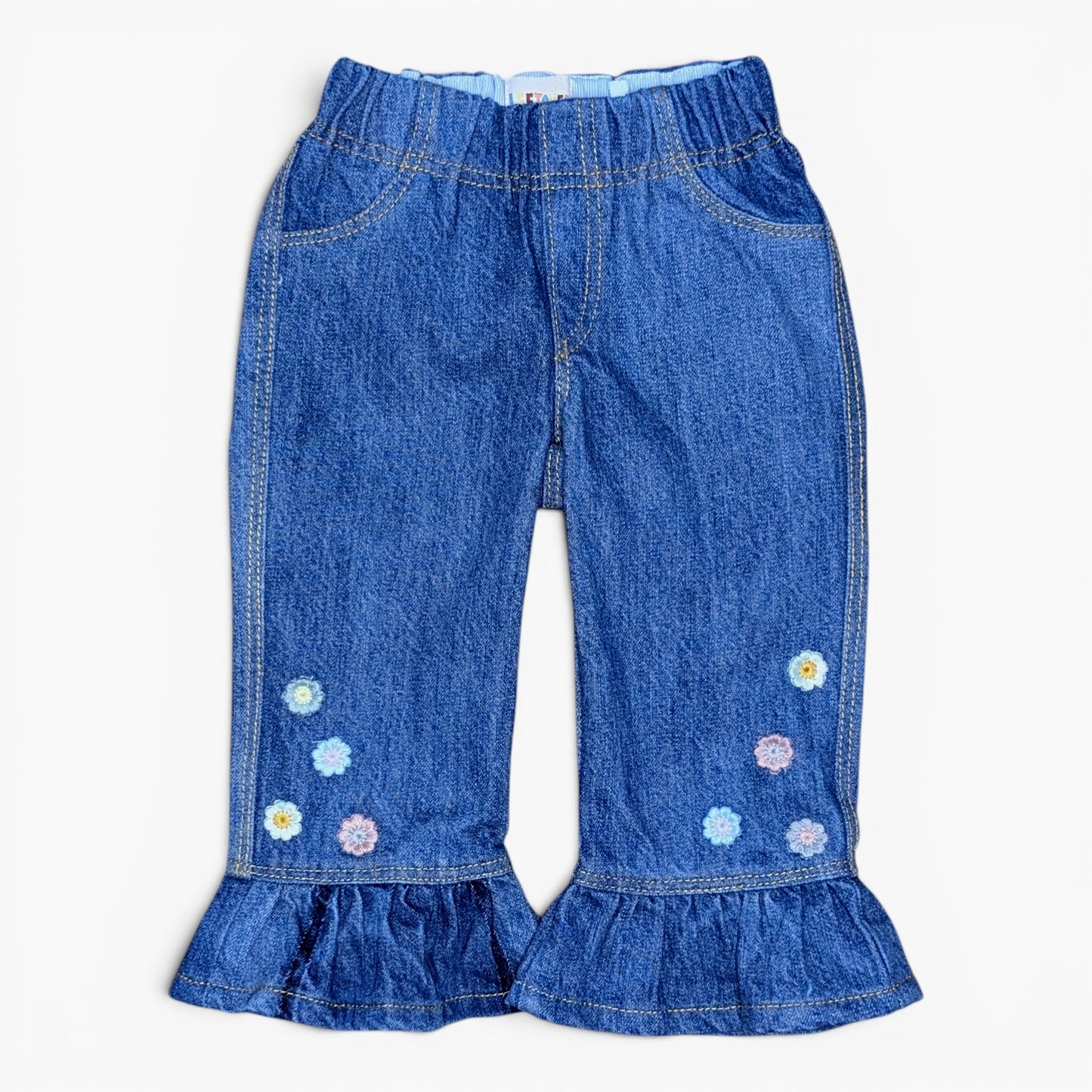 Blue denim pants with a ruffled hem, side pockets, and embroidered daisy flowers on the lower legs, shown flat on a white background.