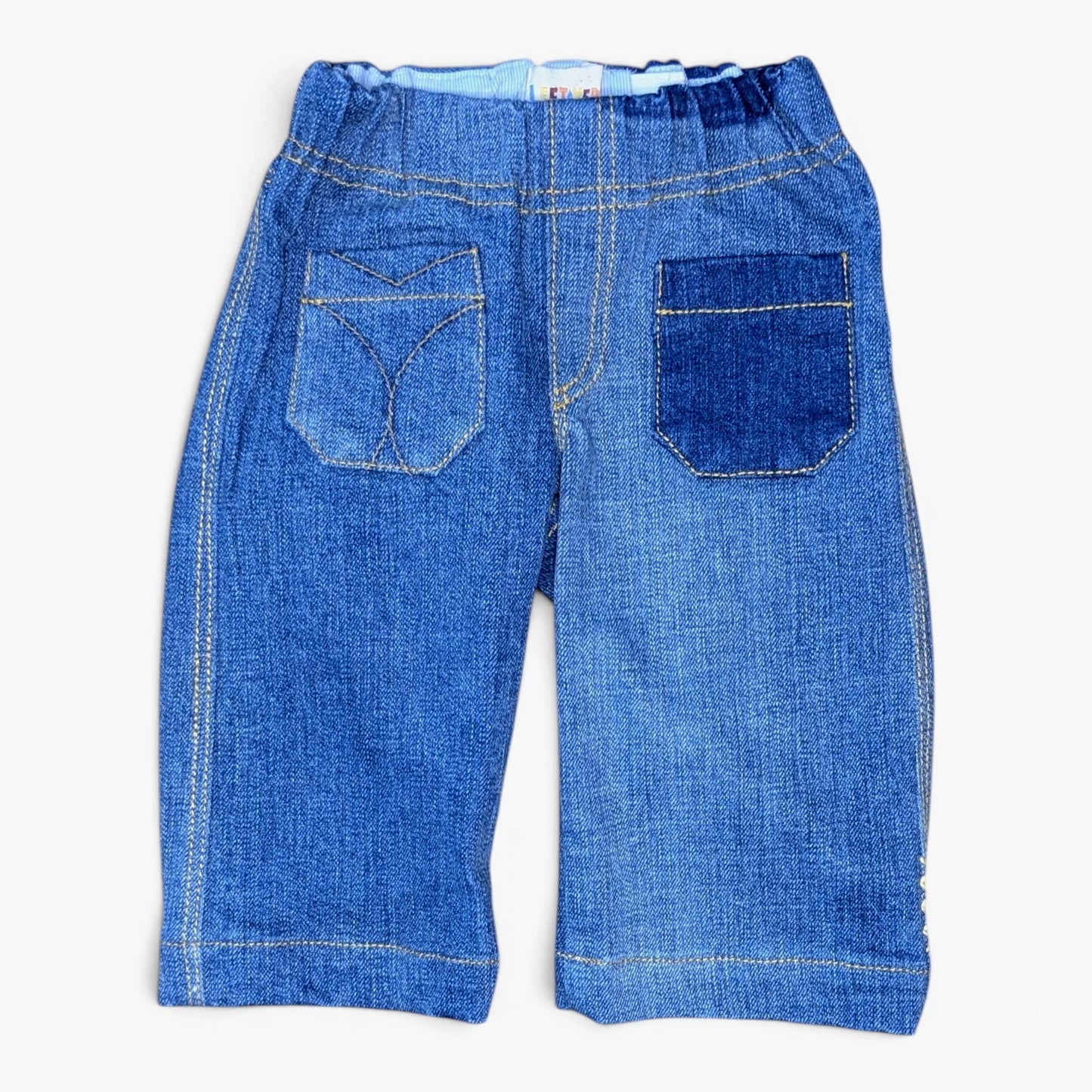 Back view of a pair of blue denim pants for toddlers with a wide elastic waistband, featuring two large patch pockets with decorative stitching, photographed on a clean white background.