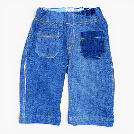 Back view of a pair of blue denim pants for toddlers with a wide elastic waistband, featuring two large patch pockets with decorative stitching, photographed on a clean white background.