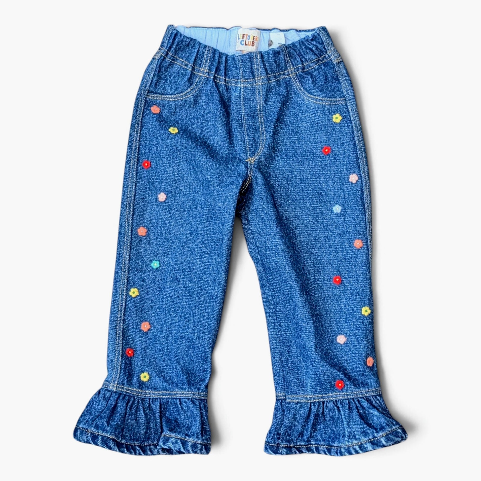 LEFTOVERS CLUB unique frankie flare Blue denim pants for kids with colorful embroidered flowers and ruffled hems, shown flat on a white background.