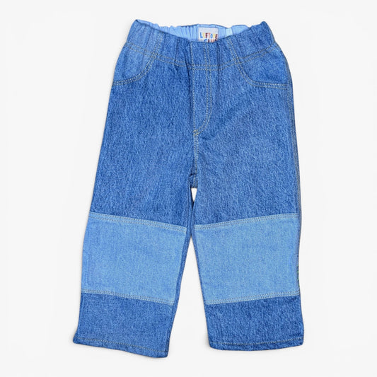Blue denim patchwork pants for kids, featuring a waistband with a small red and white brand label, front pockets, and contrasting medium and dark blue denim panels on the legs, shown against a plain white background.